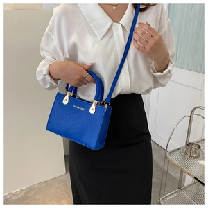 Detail of blue crocodile pattern tote bag featuring woven handle and gold hardware