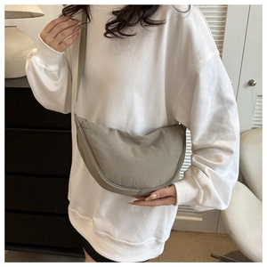 Close-up of a crescent-shaped olive nylon crossbody bag worn by a model in soft lighting
