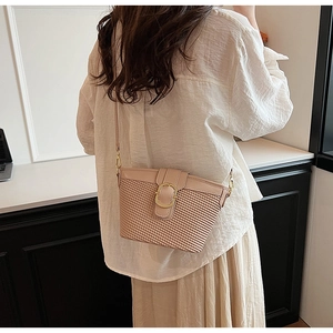 Close-up of beige crossbody bag with woven texture and a gold circular metal clasp