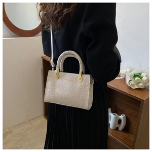 Detail of light beige crocodile embossed handbag with woven handle and gold fashion logo