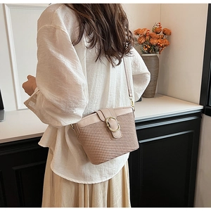 Detail of beige woven bucket bag with elegant gold ring buckle on model shoulder