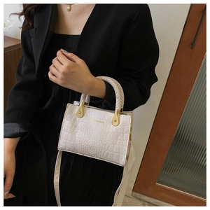 Detail of white crocodile texture bag featuring a woven handle and golden metal buckles