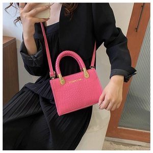 Detail of rose pink crocodile embossed handbag with woven handle and gold hardware