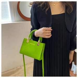 Detail of neon green crocodile texture handbag with woven handle and gold hardware