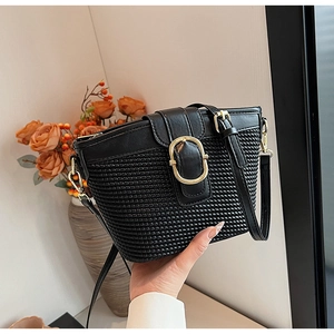 Detail of woven black bucket bag featuring gold oval buckle and leather shoulder strap