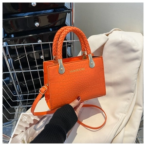 Detail of bright orange crocodile texture bag with woven handles and gold metal hardware