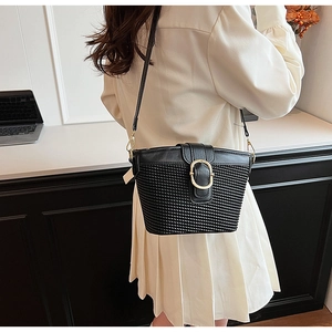 Detail of black woven leather bucket bag with gold metal buckle on a white dress