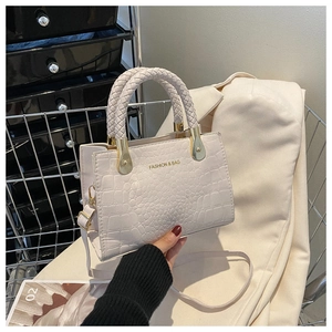Detailed close-up of white crocodile pattern leather bag with woven handles and gold metal clips