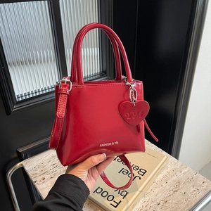 Red glossy patent leather bucket bag with top handle and heart charm in a hand-held view