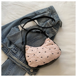 Détail du tissu plissé rose avec broderie de nœud noir sur un sac à bandoulière chic