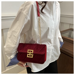 Detail of burgundy velvet crossbody bag with gold geometric buckle on a model