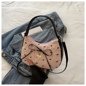 Pink pleated handbag with black bows and metal heart pendant over blue denim
