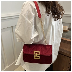 Detail of burgundy velvet crossbody bag with golden H-clasp and chain strap worn by model