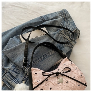 Detail of pink pleated handbag with black bows and silver heart charm on denim fabric