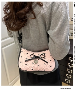Detail of pink crescent bag with black bow patterns and metal heart pendant detail