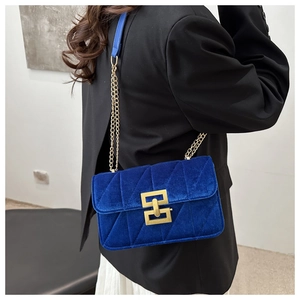 Blue velvet crossbody bag with quilted rhombic pattern and gold chain strap on shoulder