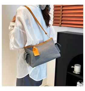 Detail of dark grey denim shoulder bag with contrasting orange leather strap and trim