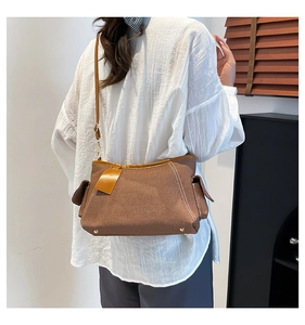 Detailed side view of a brown canvas shoulder bag with white stitching and flap pocket