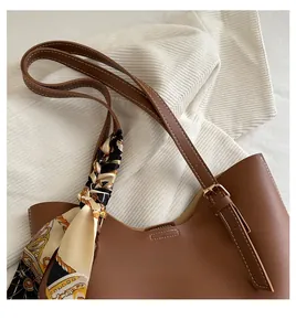 Detail of a dark brown leather tote bag with elegant silk scarf wrap and metal buckles