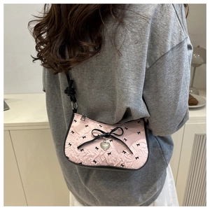Vue détaillée du sac à bandoulière rose avec motifs de nœuds noirs et pendentif cœur