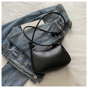 Detail of black PU leather half-moon bag with knotted strap on denim jacket background
