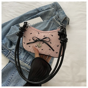 Détail du sac à bandoulière rose avec imprimé nœuds noirs et pendentif cœur