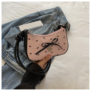 Détail du tissu froncé rose avec motifs de nœuds noirs et breloque cœur sur le sac à main