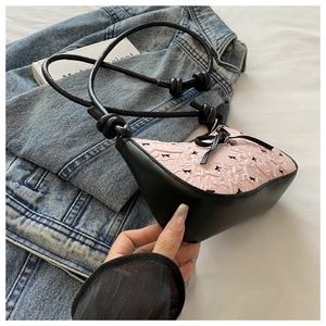 Détail du sac à bandoulière rose et noir avec nœud texturé sur fond de jean bleu
