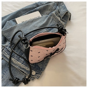 Sac bandoulière rose à nœuds avec bandoulière nouée montrant l'espace pour téléphone et portefeuille