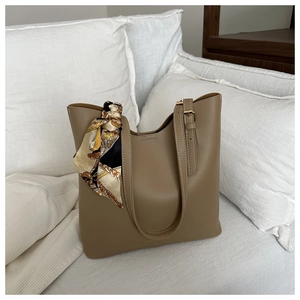 Detail of khaki leather tote bag featuring a decorative silk scarf and gold buckles