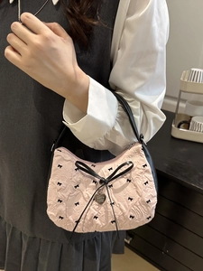 Pink pleated handbag with black bow embroidery and heart pendant shown in lifestyle setting