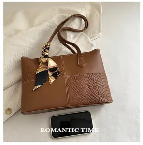 Detail of brown tote bag with crocodile texture and silk scarf handle on beige fabric