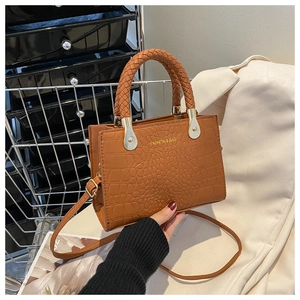 Detail of brown crocodile pattern handbag featuring a woven handle and gold hardware