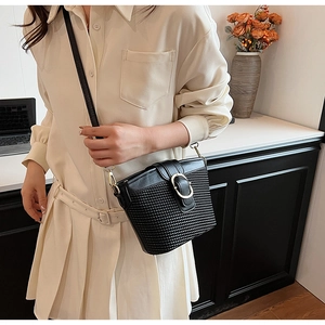 Detail of a black woven crossbody bag featuring a golden circular buckle on a model