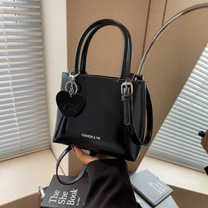 Minimalist black leather tote bag with silver logo and heart charm in a home setting