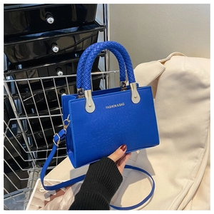 Close-up of blue croc-embossed small square bag with woven handle and gold fashion logo