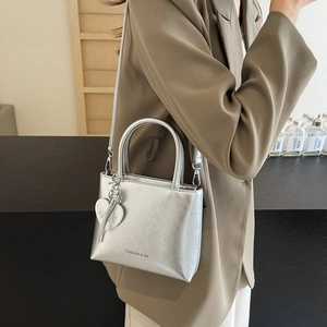 Silver metallic mini bucket bag with heart pendant worn by model in chic blazer