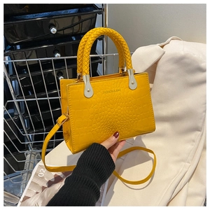Detail of yellow crocodile embossed handbag with woven handle and adjustable strap