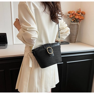 Detail of black woven shoulder bag featuring a polished gold oval metal buckle and fine texture