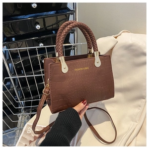 Detail of brown crocodile pattern handbag with woven handles and gold metal plate deco
