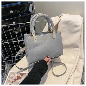 Detail of grey crocodile pattern small square bag with woven handle and gold hardware