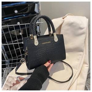 Detail of black crocodile-embossed handbag with woven handle and gold fashion lettering