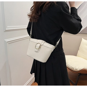 Rear view of a model wearing a white woven crossbody bag with metal circular buckle