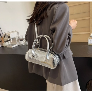 Silver metallic barrel bag with crackle finish worn as a crossbody by a model in a cafe
