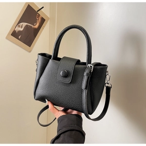 Detail of black lychee grain leather handbag with round buckle and detachable strap