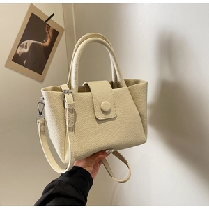 Detail of cream beige lychee textured leather bag with top handle and metal strap hooks