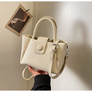 Détail de la texture cuir litchi crème et de la boucle décorative sur un sac cabas