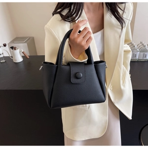 Detail of black pebbled leather handbag with handle and detachable strap on beige suit