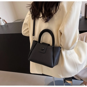 Détail du sac seau en cuir noir à motif litchi porté par un mannequin en blazer