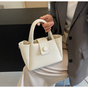 Détail du sac seau en cuir crème texturé avec une boucle métallique ronde élégante